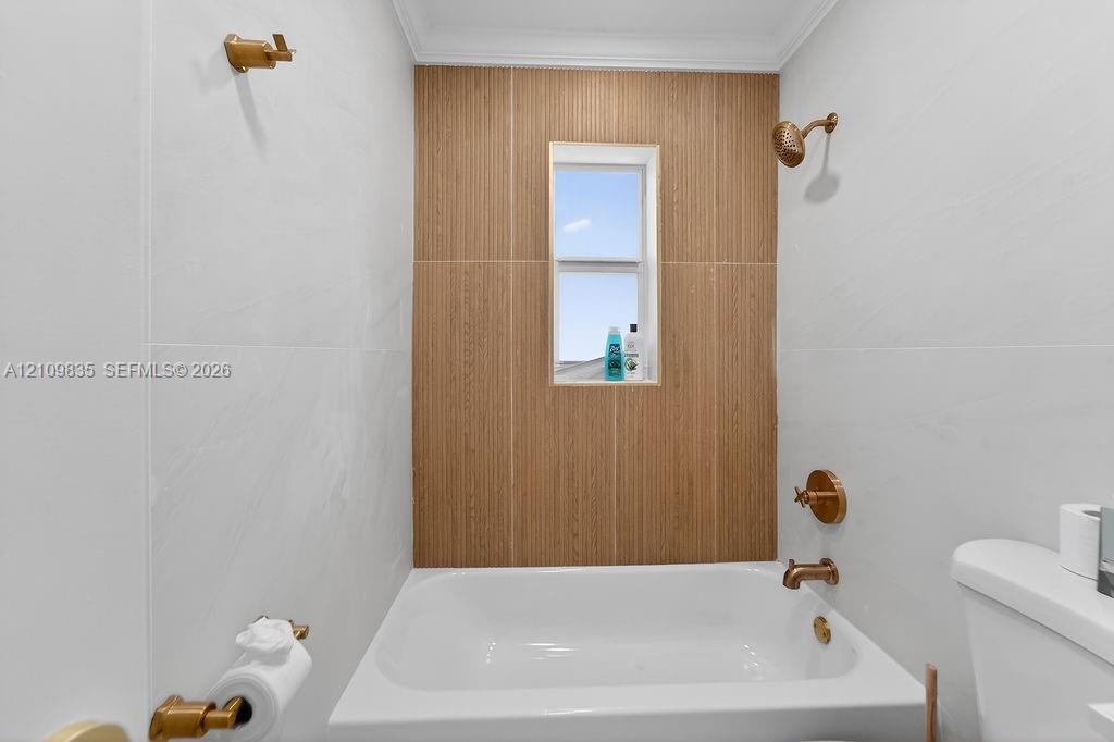 Bathtub enclosure featuring white wall tiling, a vertical wood-finish accent tile surround, and metallic-finish plumbing fixtures