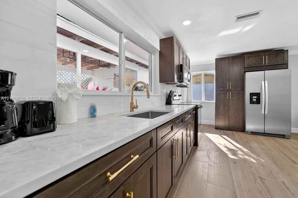 Kitchen featuring dark-finish cabinetry, stone-style countertops, wood-finish flooring, a stainless steel refrigerator, and a gold-tone faucet with an undermount sink