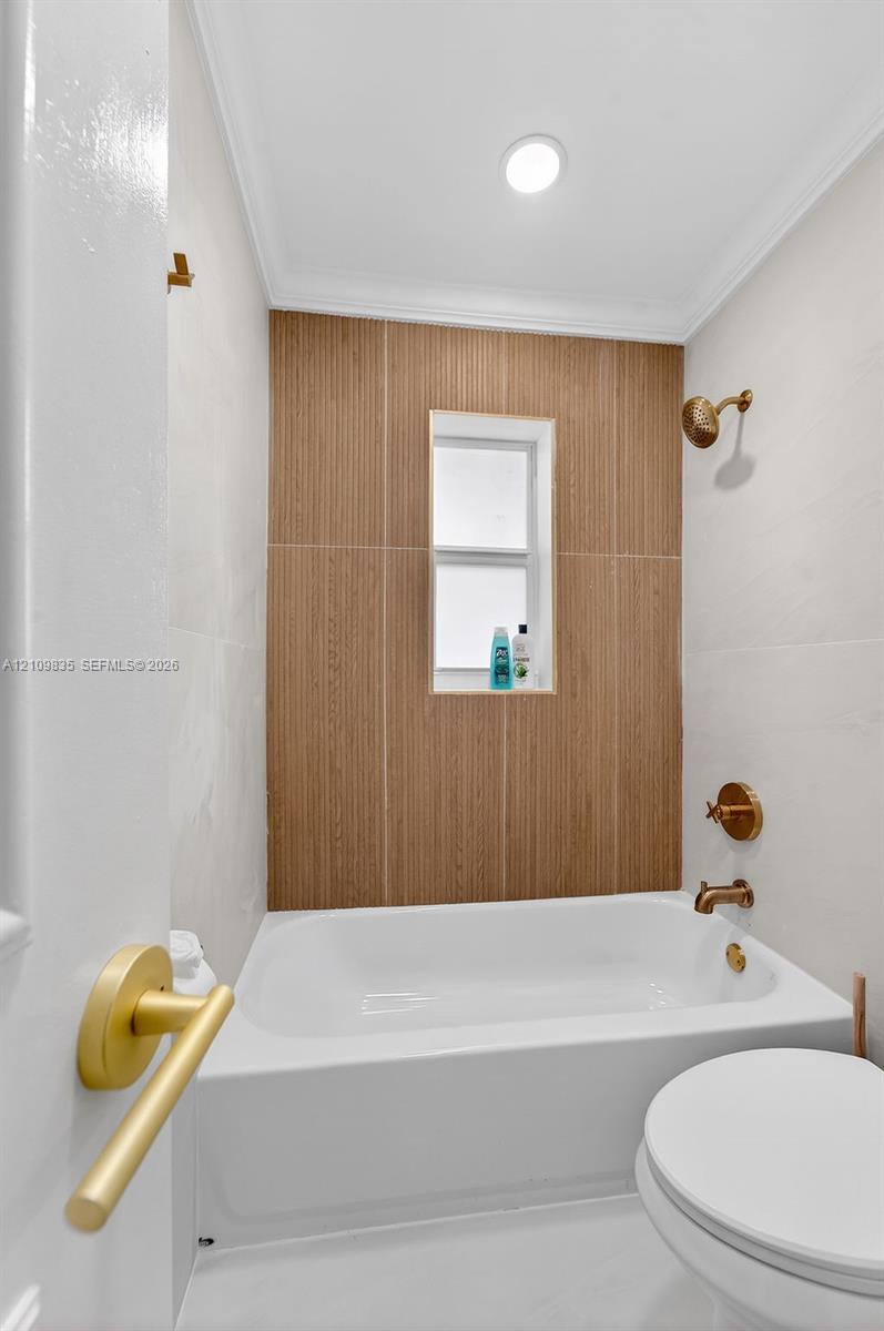 Bathroom featuring a deep soaking tub, wood-finish tile surround, recessed window niche, and brass-tone fixtures