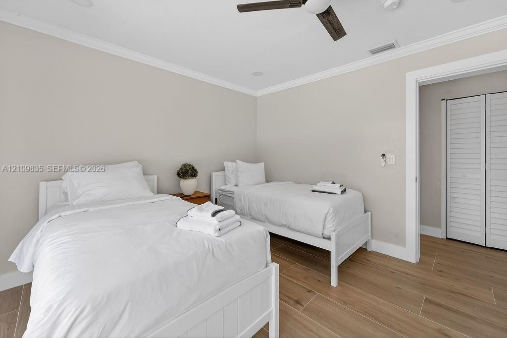 Neutral-toned room featuring wood-finish tile flooring, crown molding, a ceiling fan, and louvered closet doors