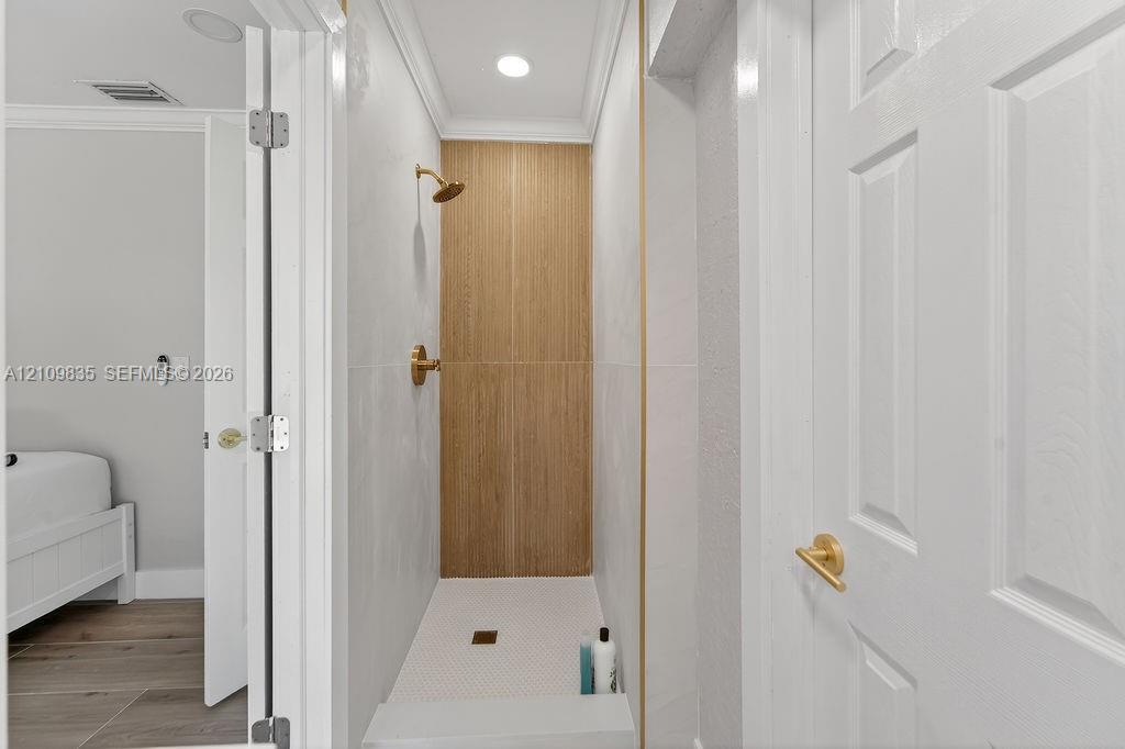 Shower stall featuring light-toned tile walls, vertical wood-finish tile accent, brushed gold shower fixture, and a mosaic tile floor