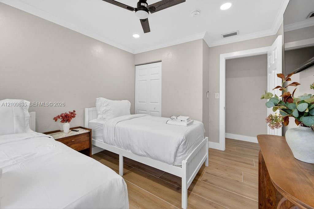 Wood-finish flooring, crown molding, ceiling fan with integrated lighting, recessed lighting, and double-door closet