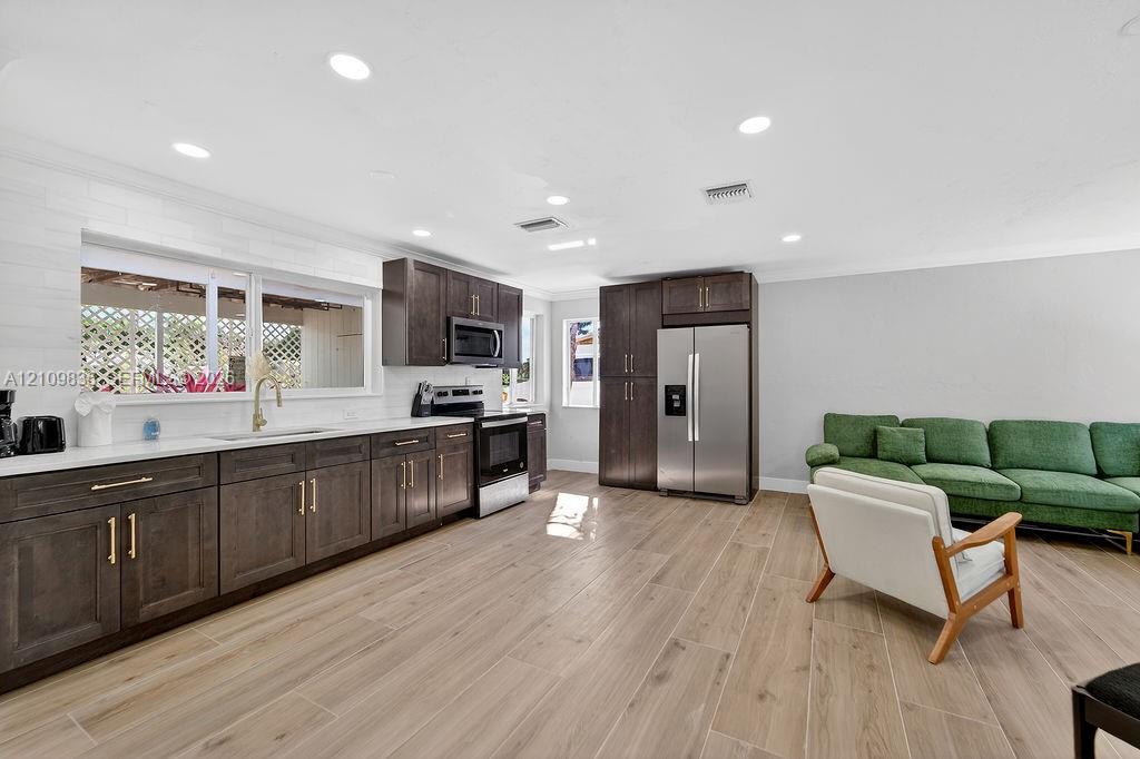 Kitchen featuring dark wood-finish cabinetry, brass-toned hardware, white countertops, stainless steel appliances, and wood-finish tile flooring