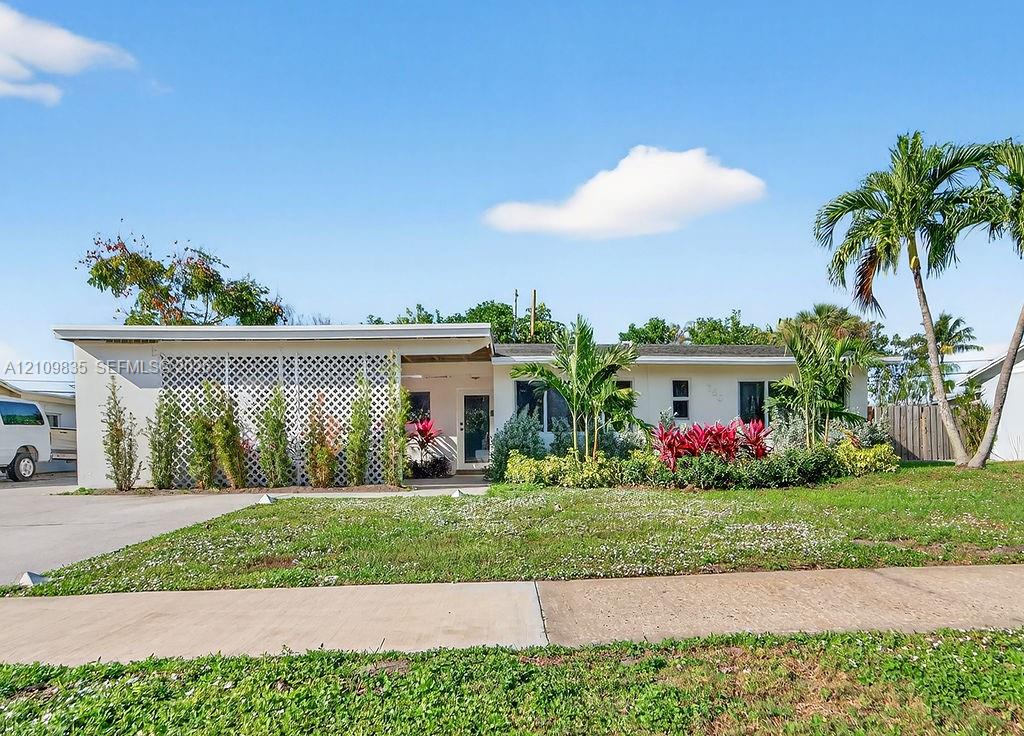 Single-story exterior featuring a white facade, decorative lattice screen, concrete driveway, and mature landscaping