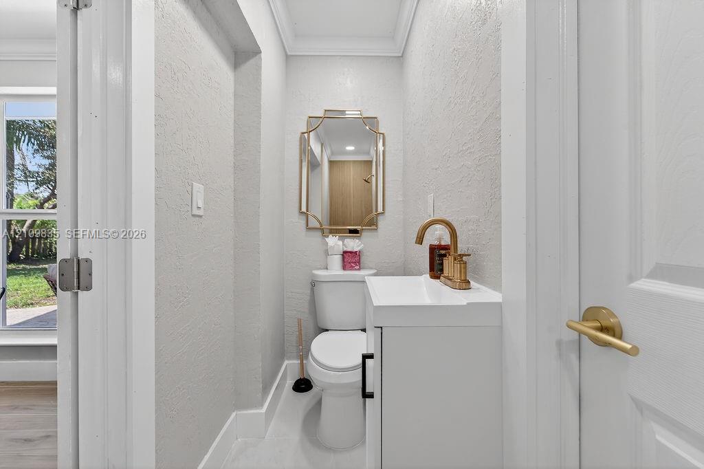 Powder room featuring a white vanity cabinet, a gold-toned high-arc faucet, a geometric-framed wall mirror, and crown molding