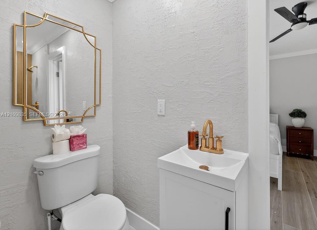 White vanity cabinet with an integrated sink basin, metallic gold faucet, geometric gold-framed mirror, and a ceiling-mounted fan