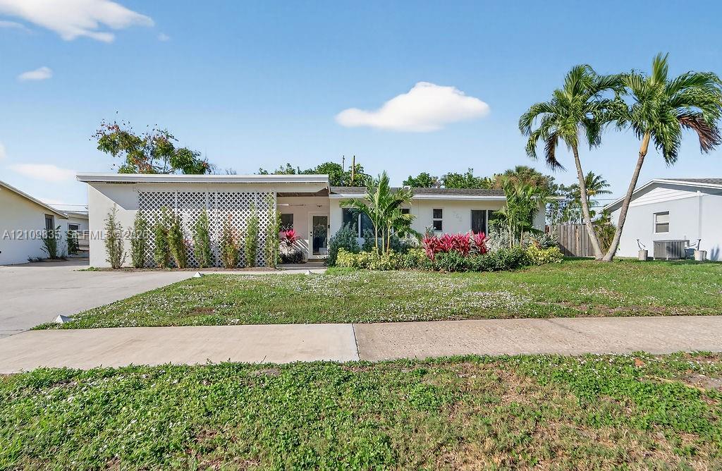 Single-story residence featuring a flat roofline, decorative lattice screen, concrete driveway, and mature palm trees Single-story residence featuring a flat roofline, decorative lattice screen, concrete driveway, and mature palm trees