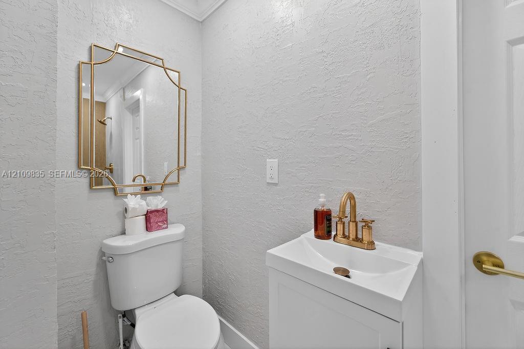 Wall-mounted vanity featuring a white basin, brushed gold widespread faucet, geometric gold-framed wall mirror, and two-piece toilet