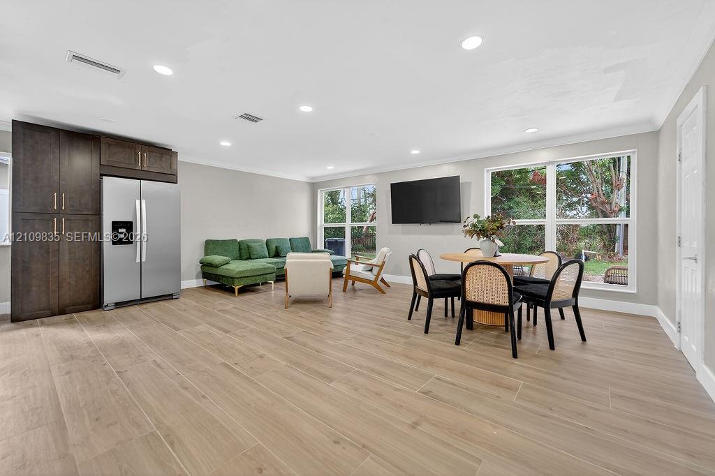 Open-concept living space featuring wood-finish tile flooring, recessed lighting, floor-to-ceiling dark wood cabinetry, and large windows