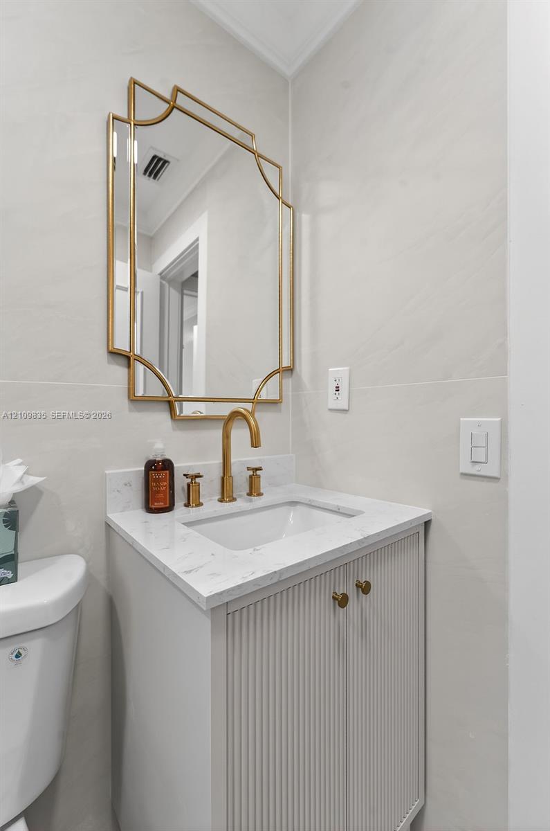 Bathroom vanity featuring a fluted cabinet base, stone-composite countertop, brushed gold faucet, and matching geometric wall-mounted mirror