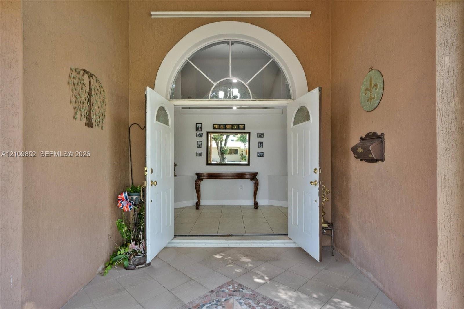 Covered entryway featuring a tiled porch and double doors with an arched fanlight window