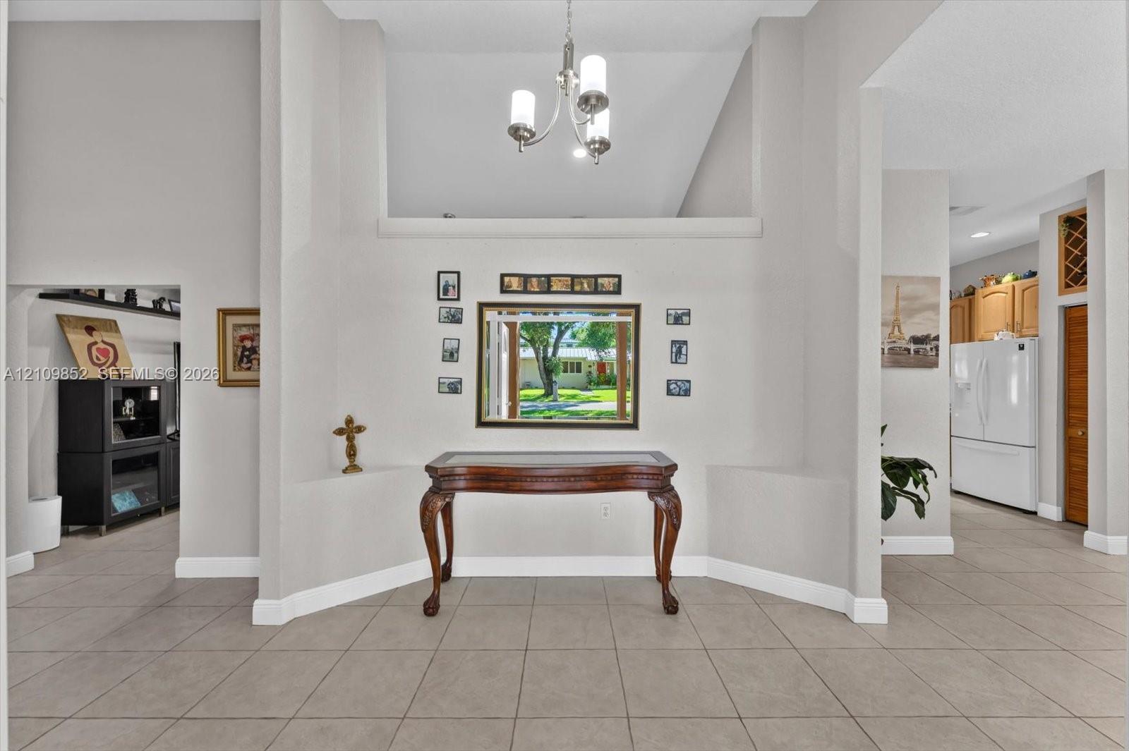 Entryway featuring volume ceilings, neutral ceramic tile flooring, a multi-arm chandelier, and a recessed wall niche *