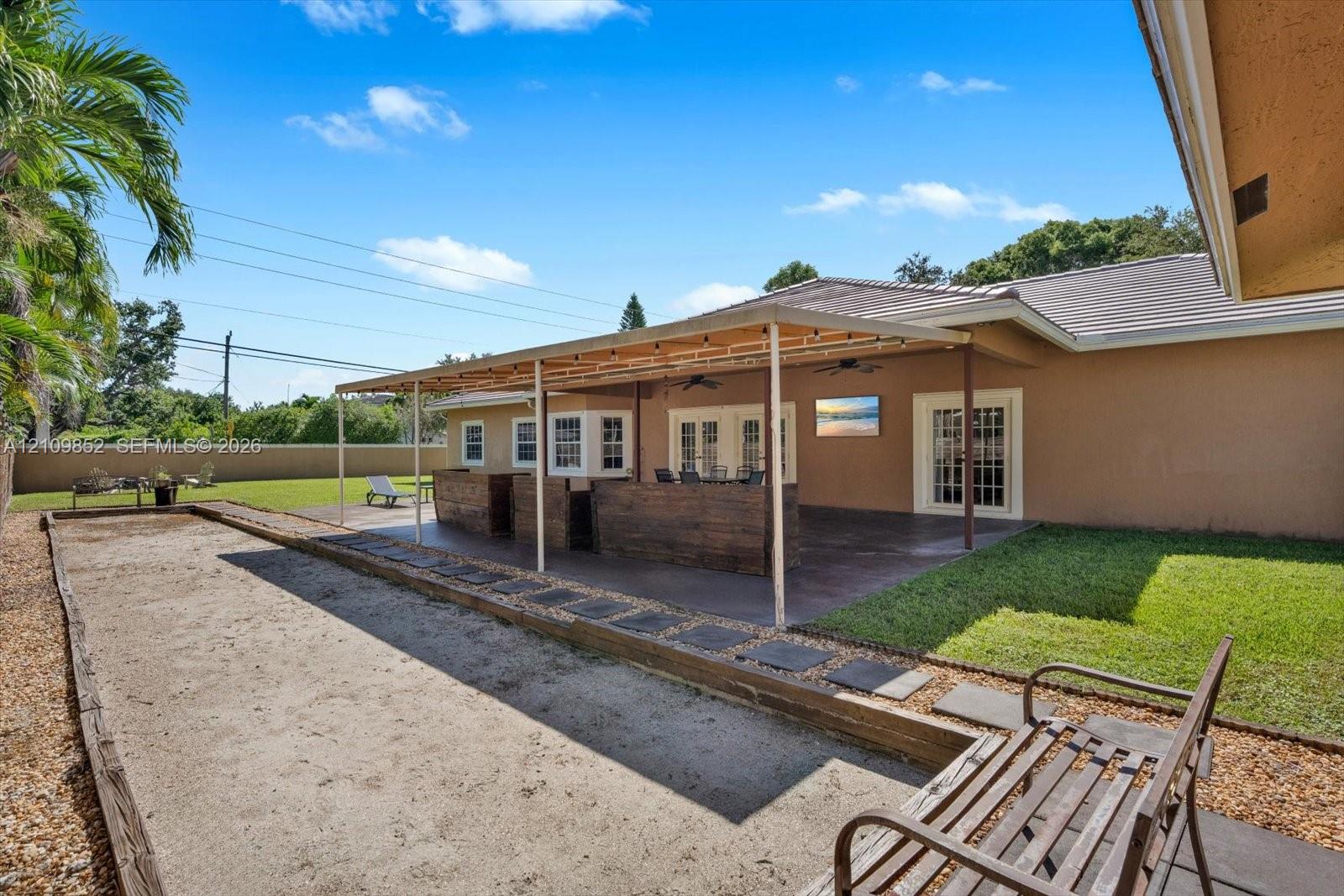 Covered extended patio featuring a concrete slab foundation, recessed ceiling fans, and a complemented by an outdoor bocce ball court and a manicured lawn *