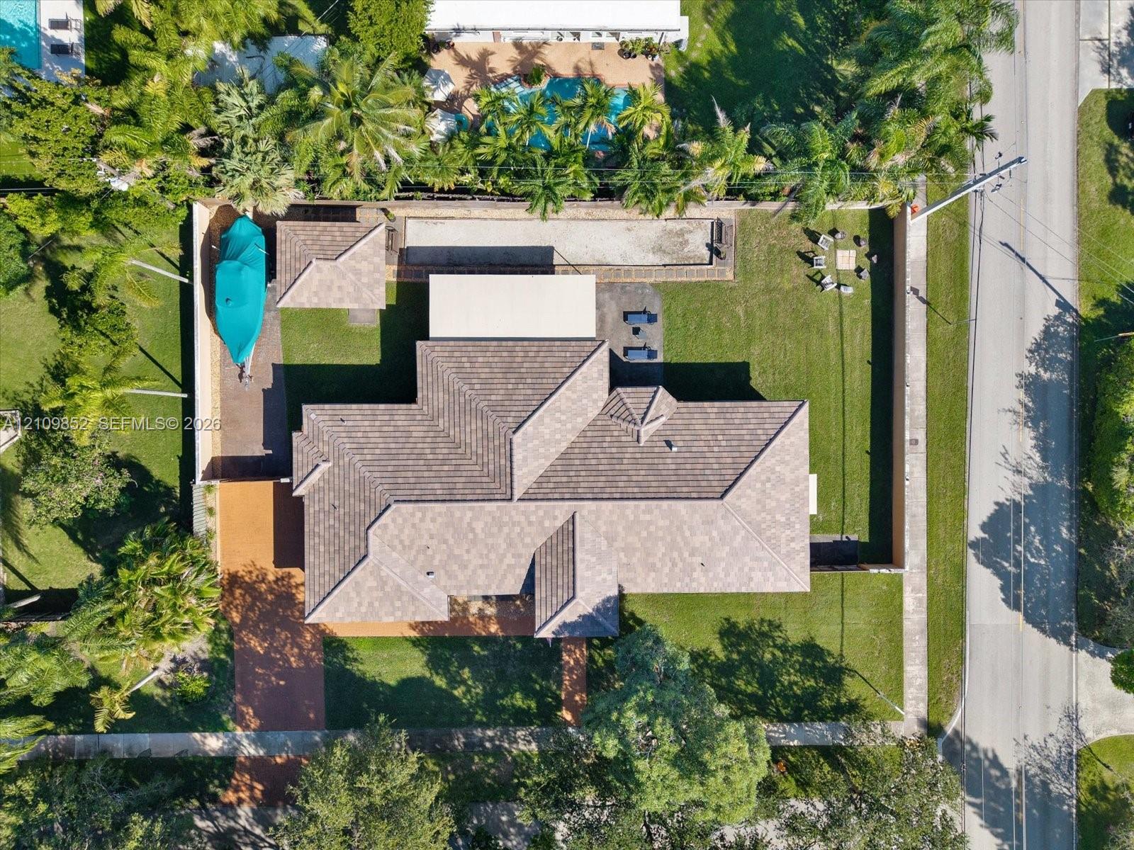 Aerial perspective featuring a multi-hipped roofline, expansive grass lawn, paved driveway, enclosed perimeter wall, and mature landscaping