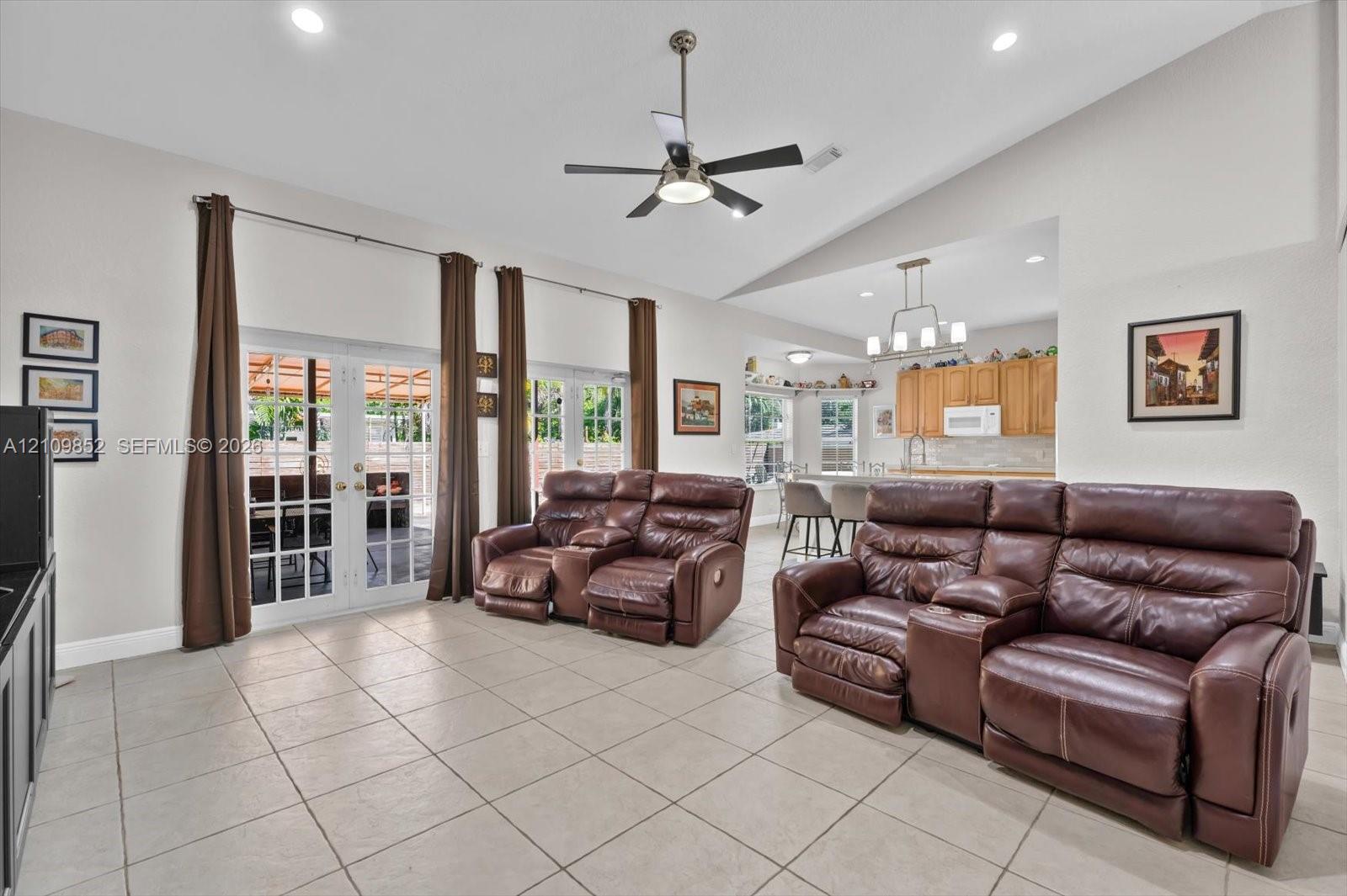 Open-concept area featuring volume ceilings, neutral ceramic tile flooring, recessed lighting, a modern ceiling fan, and dual glass-panel French doors