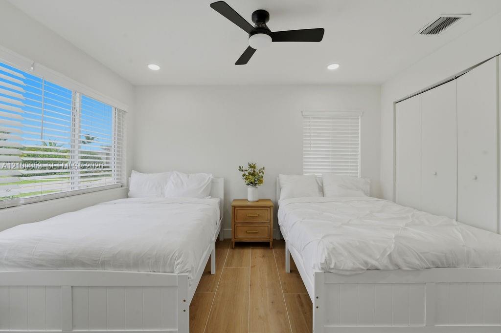 Wood-finish flooring, recessed lighting, matte black ceiling fan, dual windows with horizontal blinds, and floor-to-ceiling closet with sliding doors