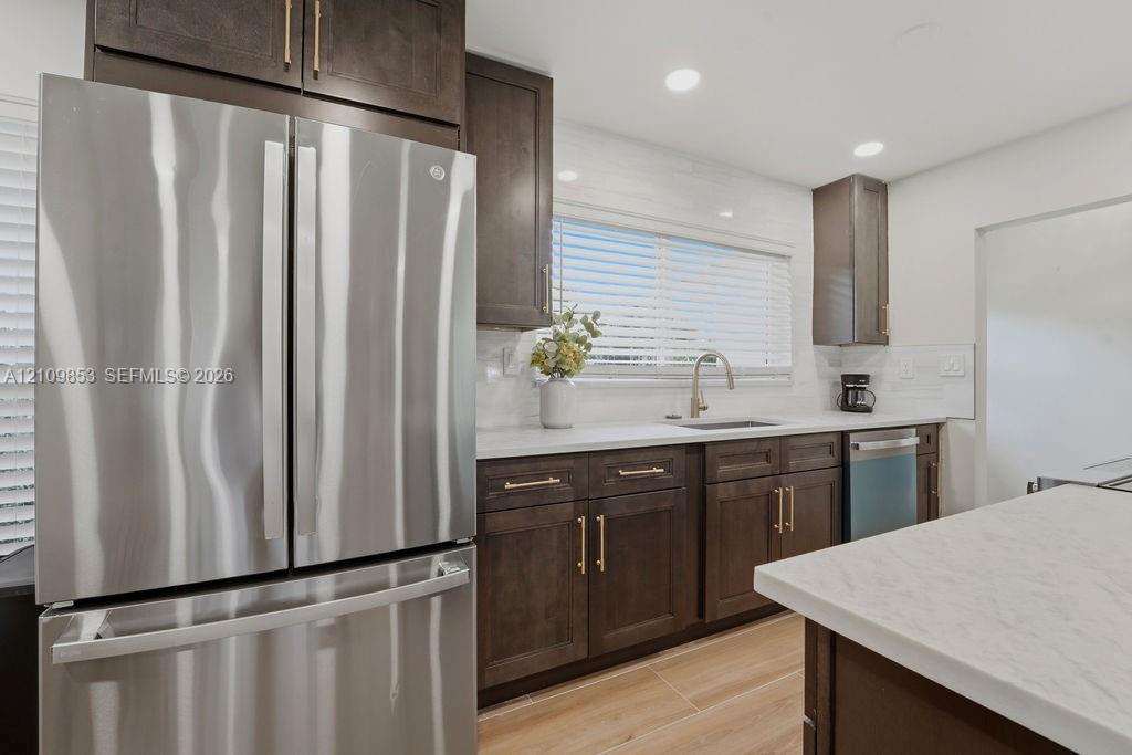 Kitchen featuring dark-finish cabinetry, stainless steel appliances, light-toned stone-finish countertops, subway tile backsplash, and wood-finish flooring