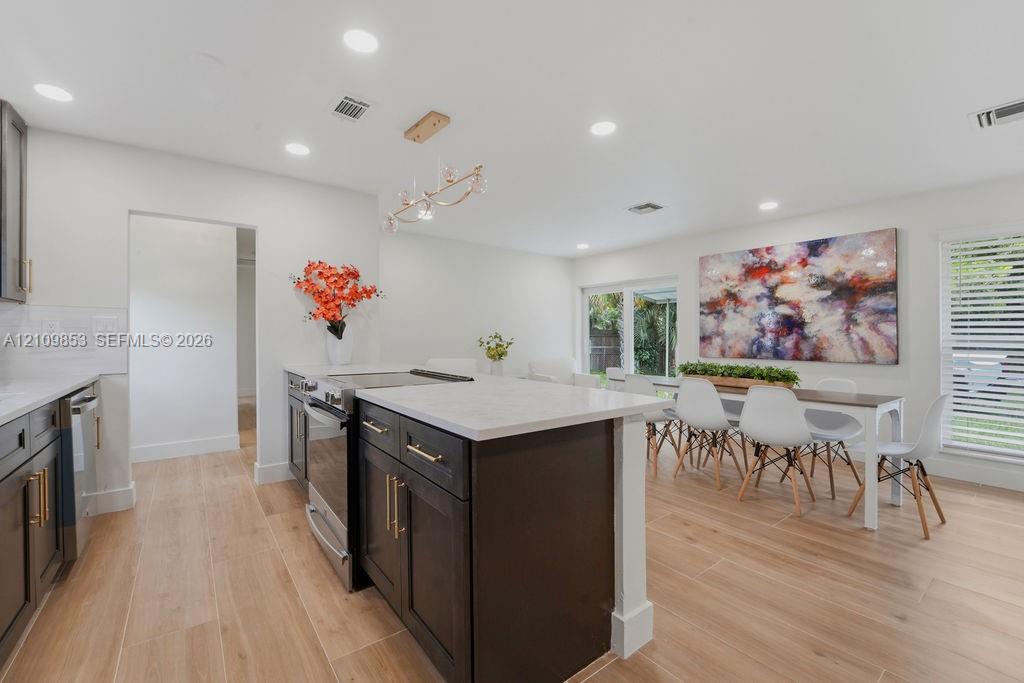 Kitchen featuring dark wood cabinetry, a central island with a stone-finish countertop, recessed lighting, wood-finish flooring, and a modern tiered chandelier