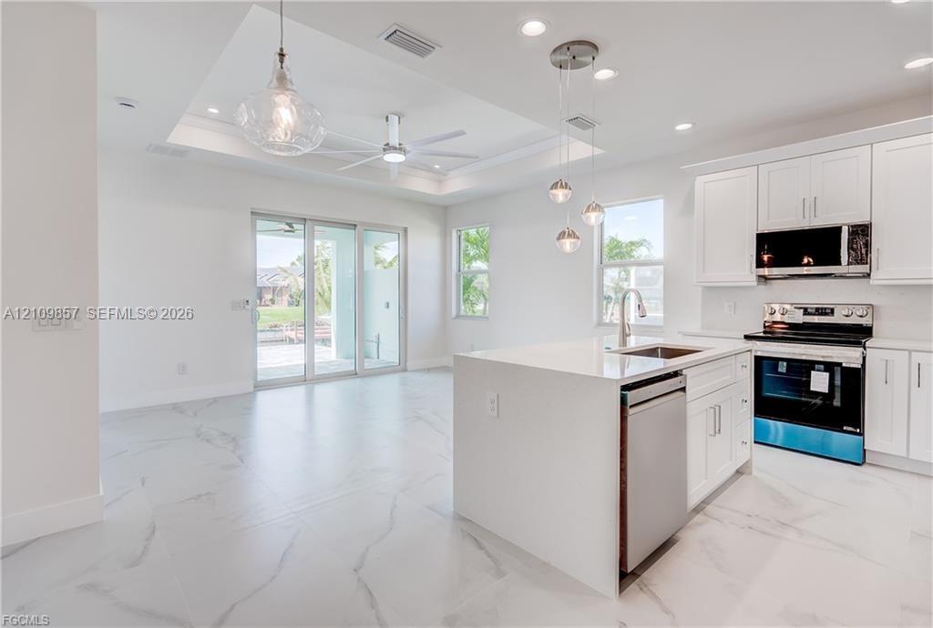 Kitchen featuring white cabinetry, a center island with a stone-finish countertop, stainless steel appliances, and large-format tile flooring with a marble pattern, capped with a tray ceiling and recessed lighting