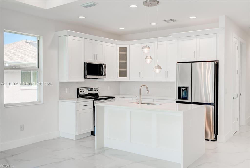 Kitchen featuring white shaker-style cabinetry, a central island with a waterfall edge, stone countertops, stainless steel appliances, and pendant lighting