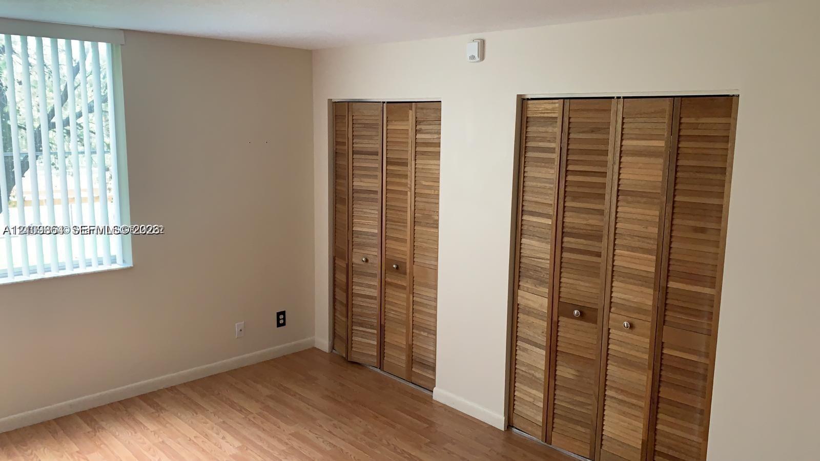 Room featuring wood-finish flooring, two sets of bifold louvered closet doors, and vertical window blinds