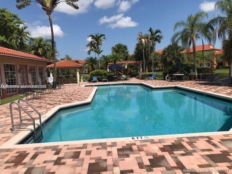 In-ground swimming pool with a paved deck, terracotta tile roof structures, and mature palm trees