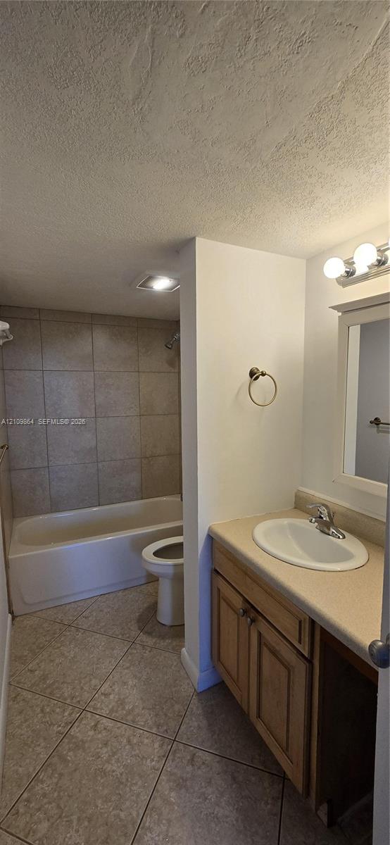 Bathroom featuring large-format tile flooring, wood-finish cabinetry, an integrated vanity countertop with a drop-in sink, and a shower-tub combination with tiled surround