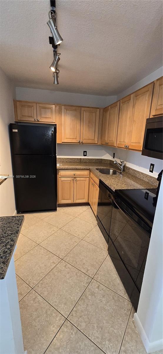 Kitchen featuring wood cabinetry, stone-surface countertops, black appliances, tile flooring, and adjustable track lighting