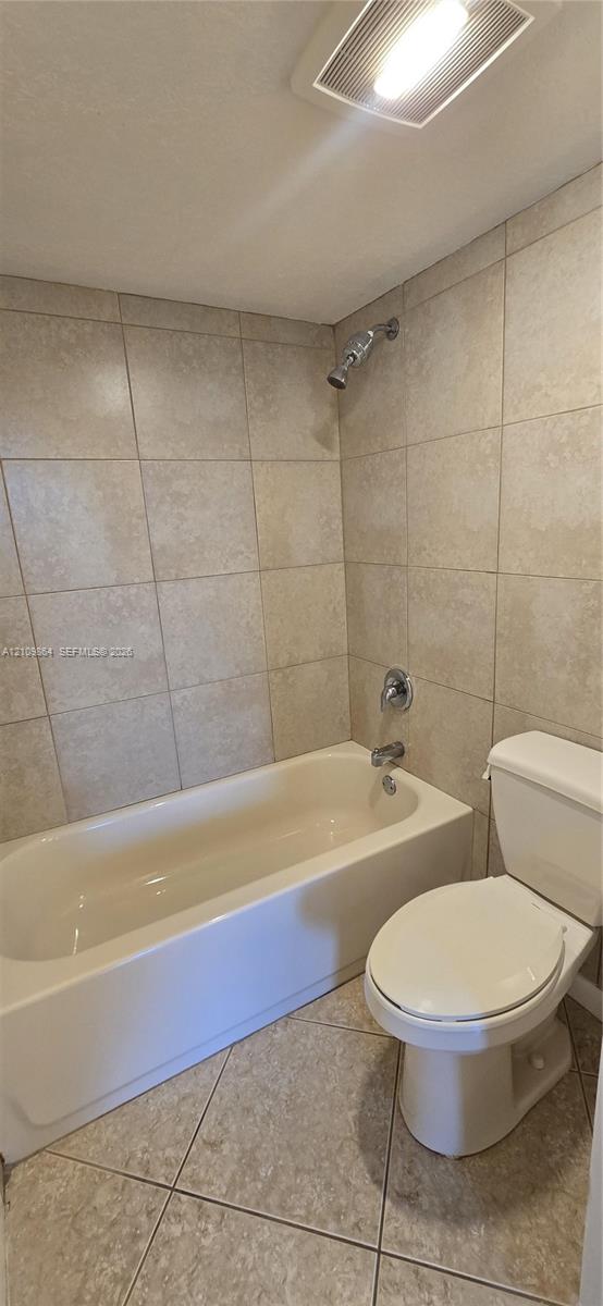 Bathroom featuring a porcelain soaking tub, neutral tile surround, ceramic floor tiling, and wall-mounted light fixture
