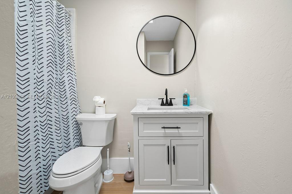 White shaker-style vanity with a stone-composite countertop, integrated sink, matte black faucet, and circular wall-mounted mirror