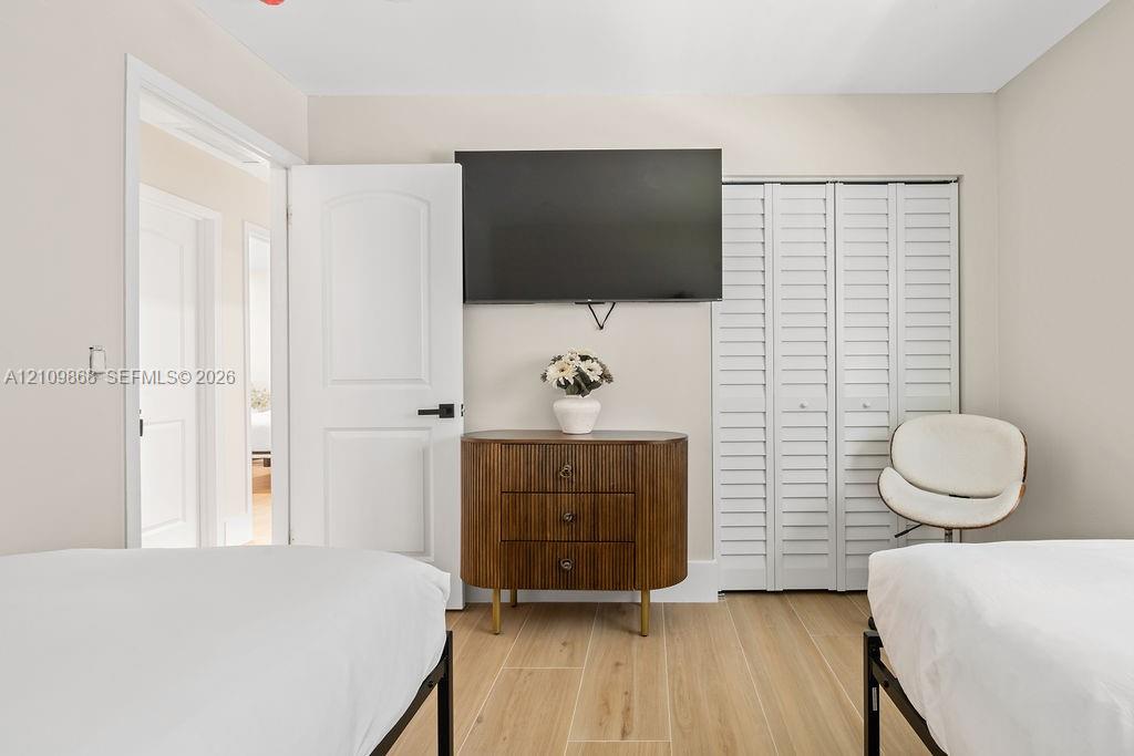 Neutral-toned interior featuring wood-finish flooring, white louvered closet doors, and a solid-core interior door with matte black hardware