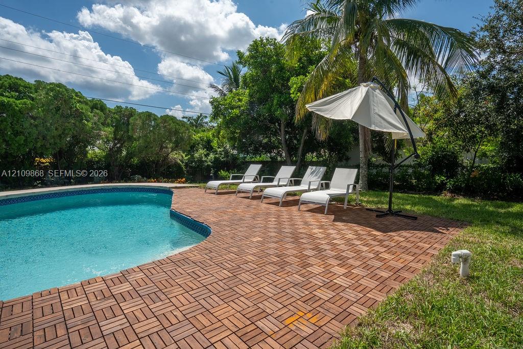 Swimming pool with a curved edge, finished with modular wood-style deck tiles, surrounded by a lawn and mature perimeter landscaping