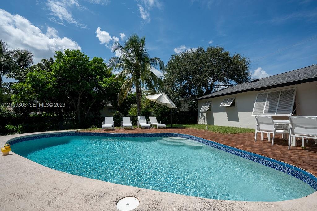 In-ground swimming pool featuring tile coping and integrated steps, surrounded by a paved brick patio and concrete decking