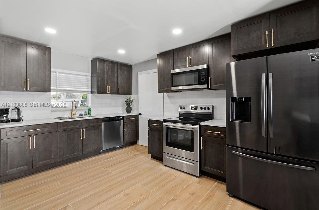 Kitchen featuring dark wood-finish cabinetry, quartz countertops, stainless steel appliances, and wood-finish tile flooring