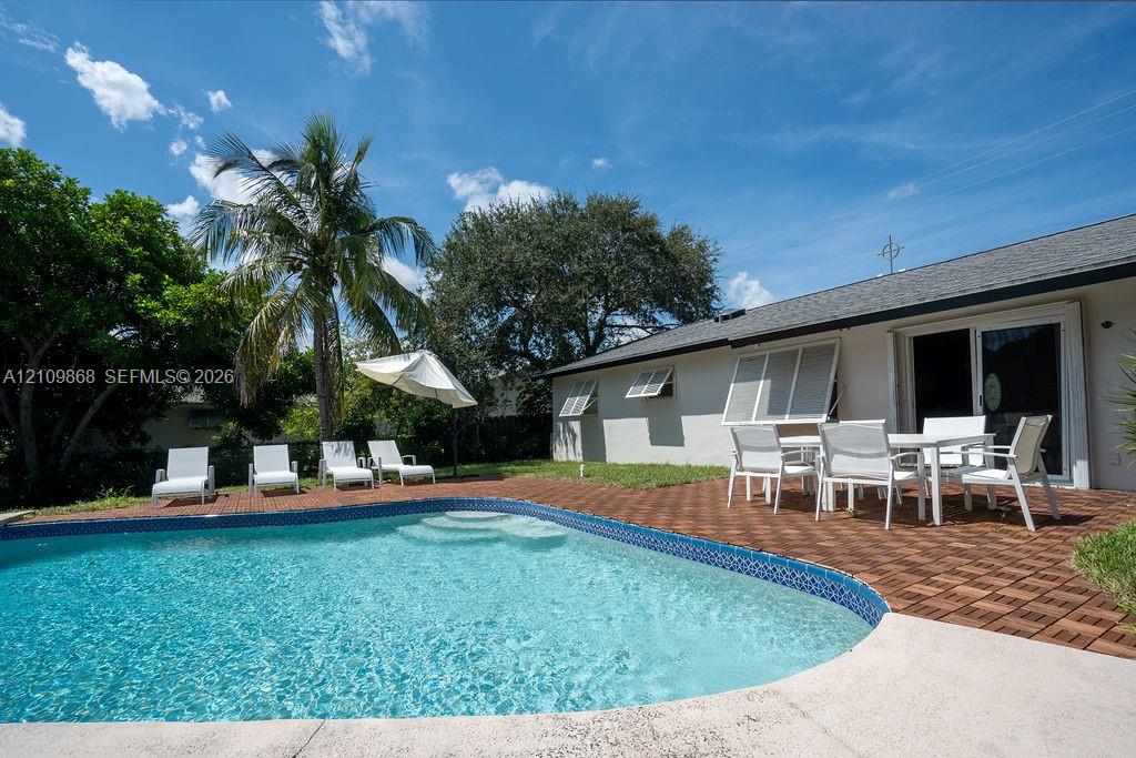 In-ground swimming pool featuring a curved design and integrated stairs, complemented by a patio area with interlocking wood-finish tiles and exterior shutters