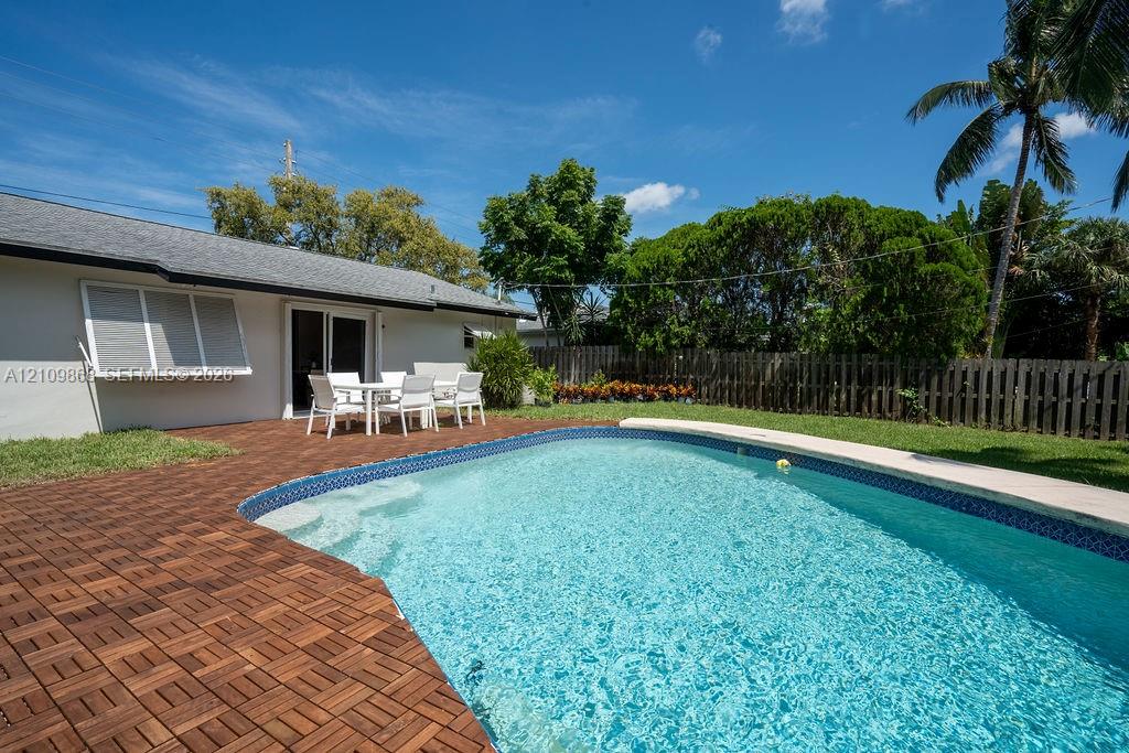In-ground pool with stone-tiled edging, custom wood-tile patio decking, wood-plank perimeter fencing, and mature landscaping