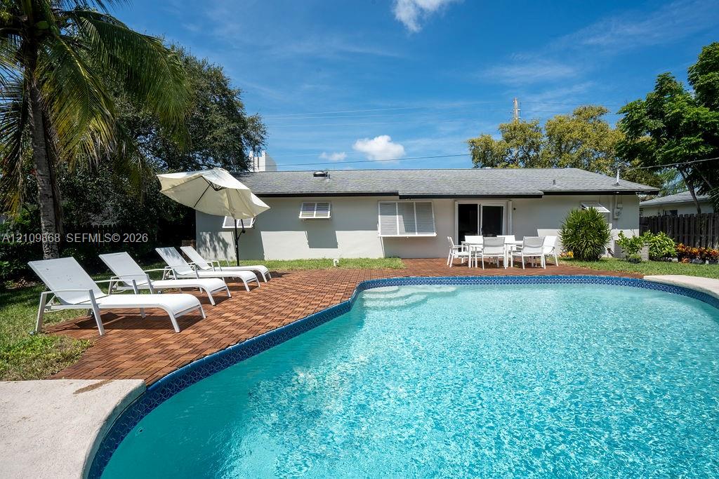 Backyard featuring a swimming pool, brick-paver decking, perimeter fencing, and mature landscaping