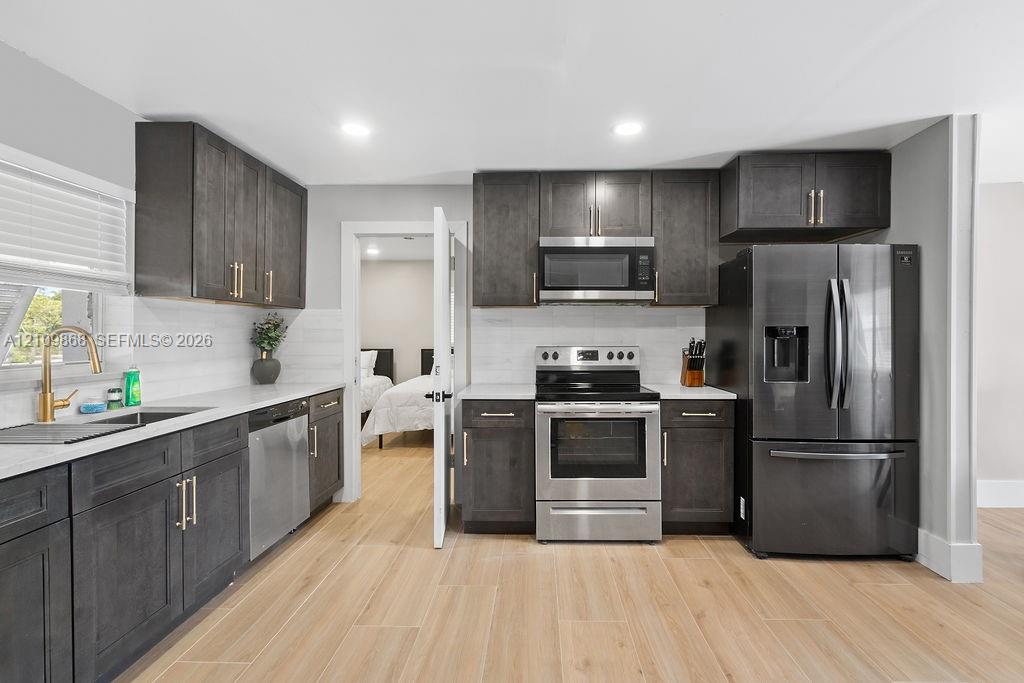 Kitchen featuring dark-stained cabinetry, wood-finish flooring, quartz countertops, stainless steel appliances, and a gold-tone faucet