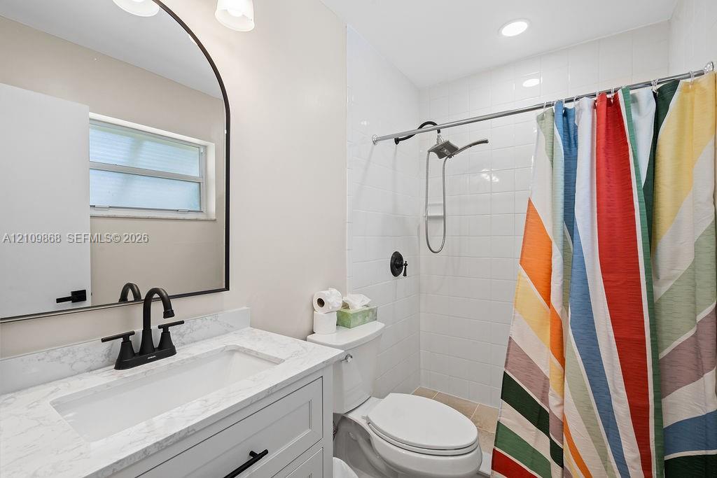 Bathroom featuring a stone-look countertop vanity with a matte black faucet, a rounded arch mirror, and a tub-shower combination with white subway tile surround and matte black fixtures
