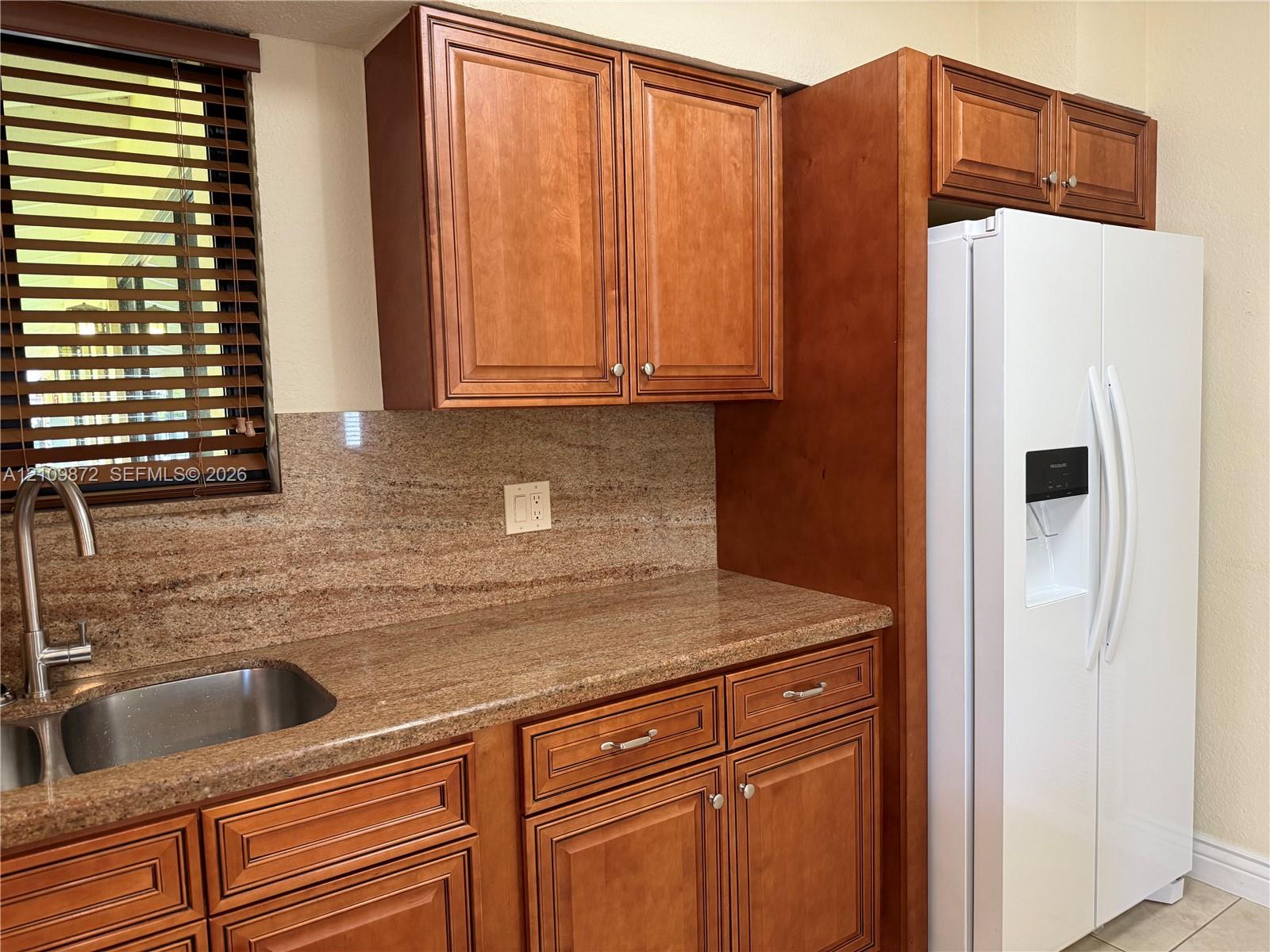 Kitchen featuring natural-finish wood cabinetry, stone-surface countertops, matching stone backsplash, stainless steel under-mount sink, and gooseneck faucet