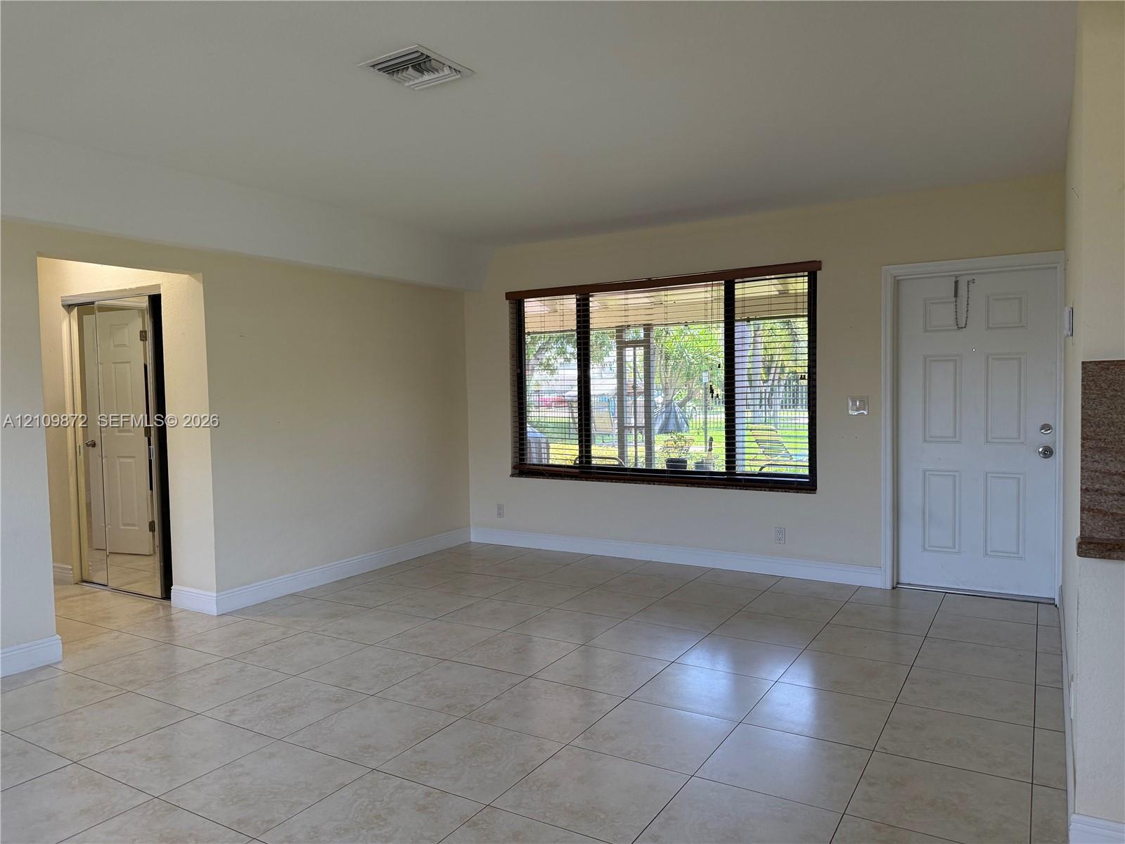Neutral-toned ceramic tile flooring, expansive window with dark trim, multi-panel exterior entry door, and a built-in mirrored closet door