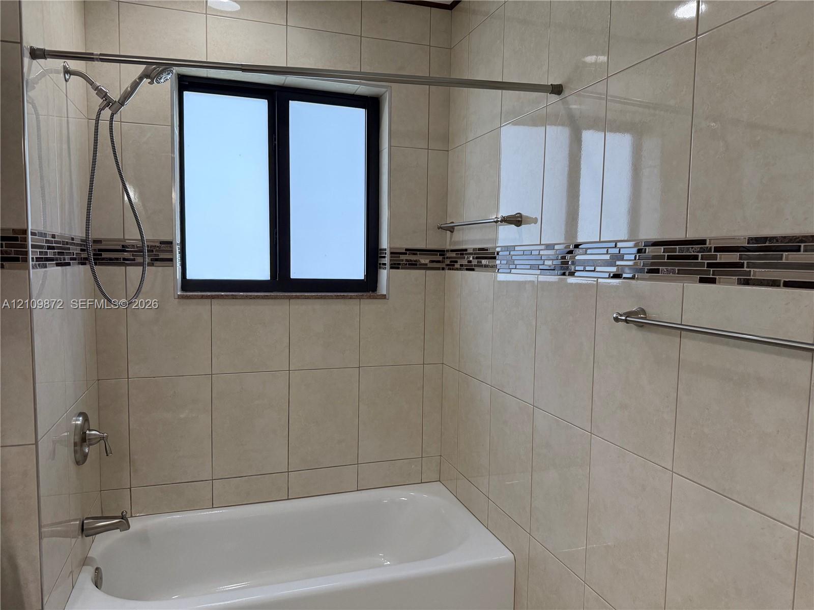 Full-height tile shower surround featuring a decorative mosaic tile accent border, inset window, brushed nickel plumbing fixtures, and integrated towel bars