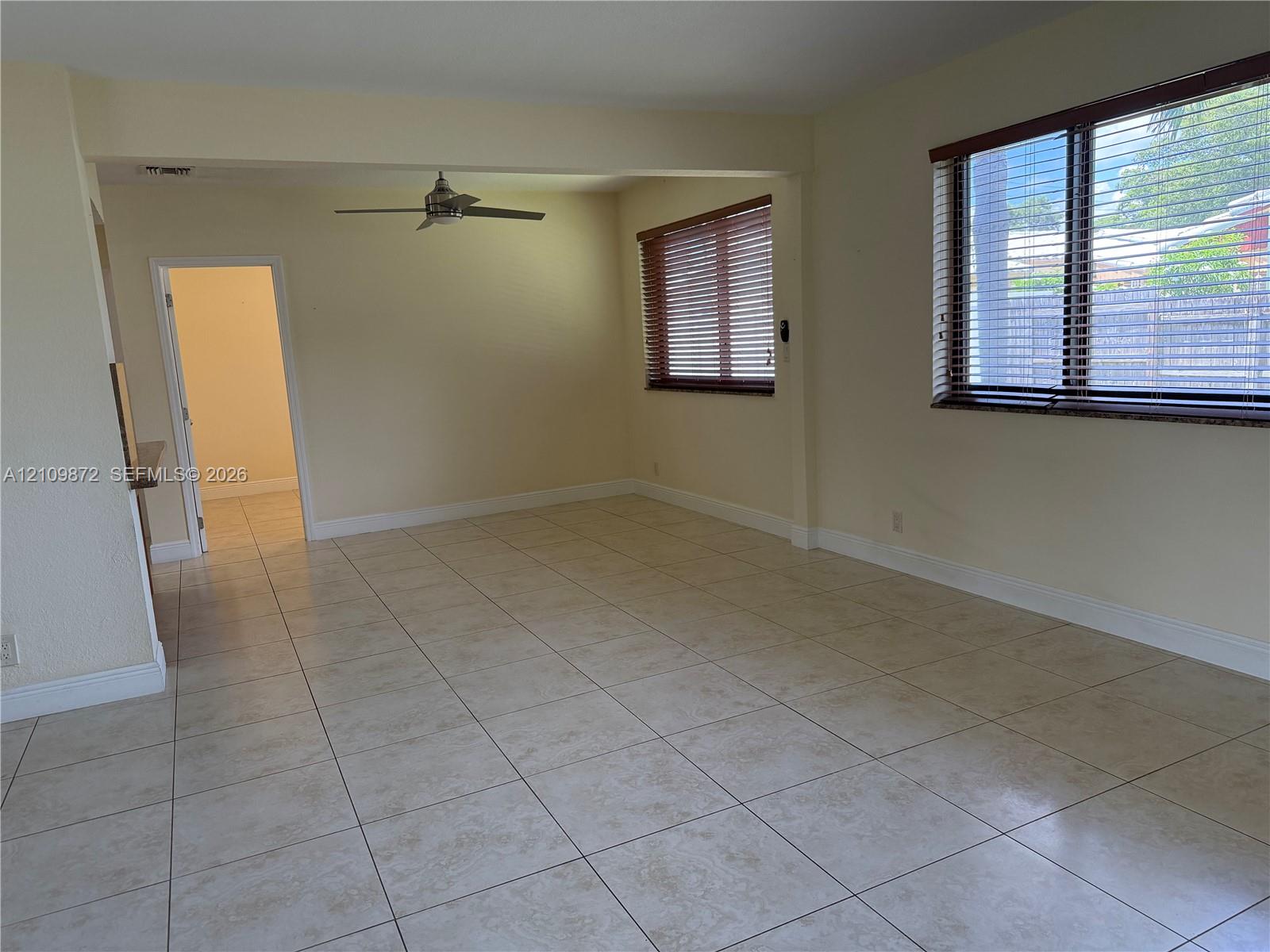 Interior space featuring neutral tile flooring, multiple windows with horizontal blinds, and a ceiling fan