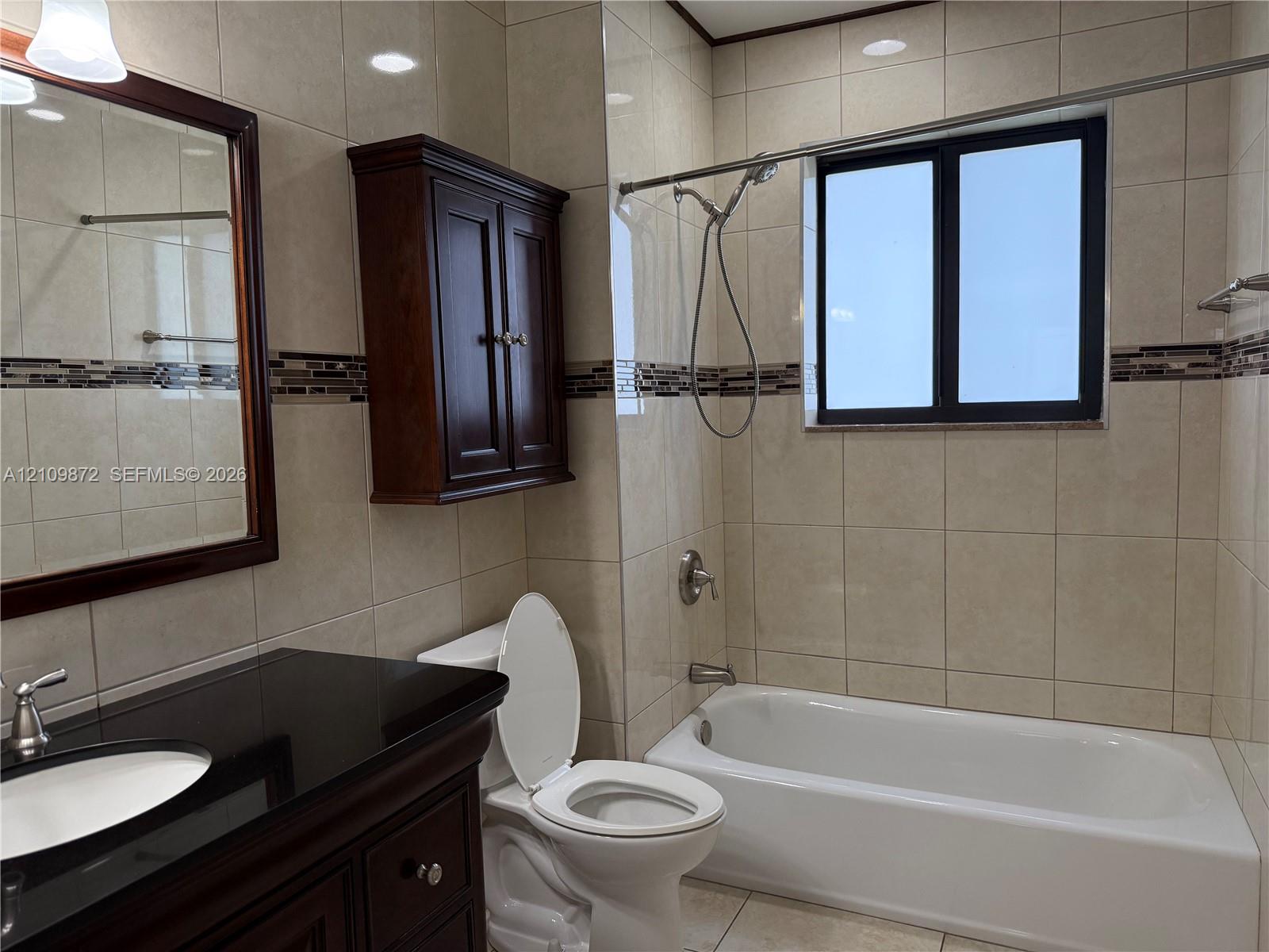 Bathroom featuring large-format wall tiling with a mosaic accent strip, dark wood-finish vanity with a stone countertop, built-in wall cabinetry, and a bathtub with a handheld shower fixture