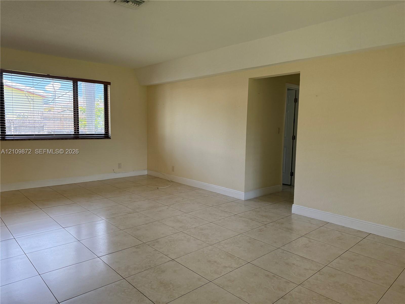 Interior space featuring large-format ceramic tile flooring, neutral wall tones, and a window with horizontal blinds