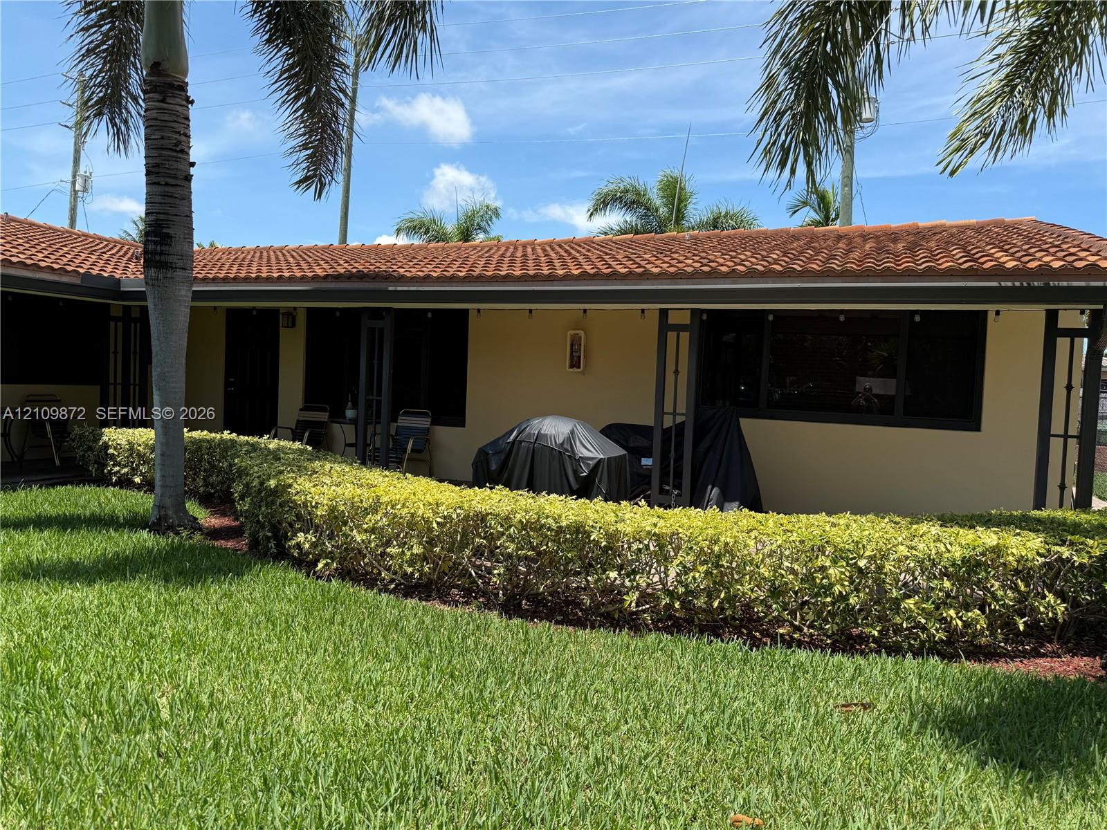 Exterior facade featuring a terracotta-style tile roof, stucco siding, and a covered concrete patio bordered by manicured hedging Exterior facade featuring a terracotta-style tile roof, stucco siding, and a covered concrete patio bordered by manicured hedging