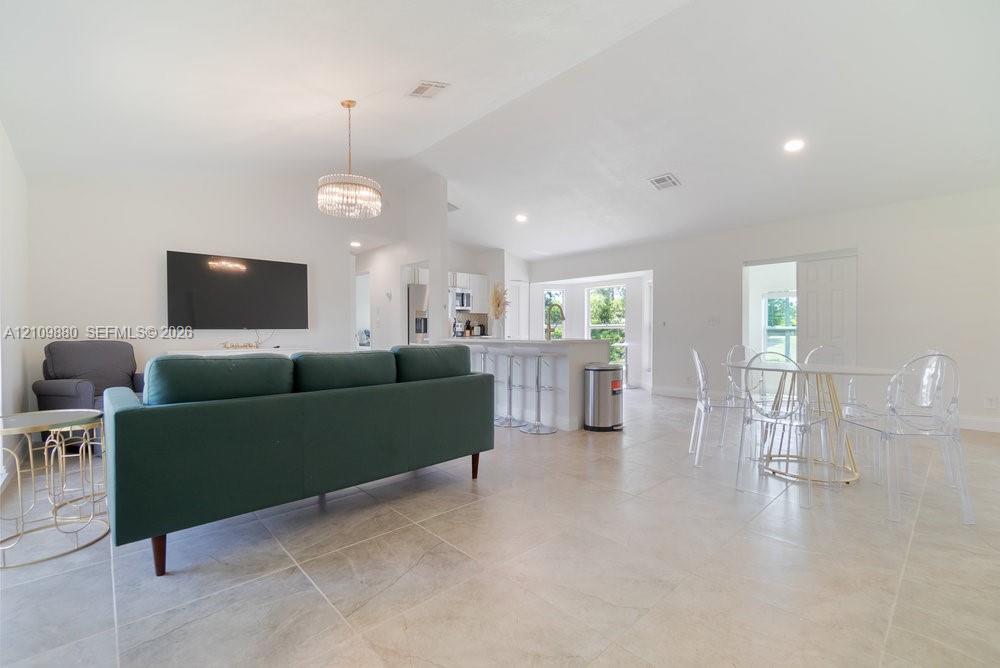 Open-concept interior featuring vaulted ceilings, oversized tile flooring, a tiered kitchen island with bar seating, and a decorative tiered chandelier
