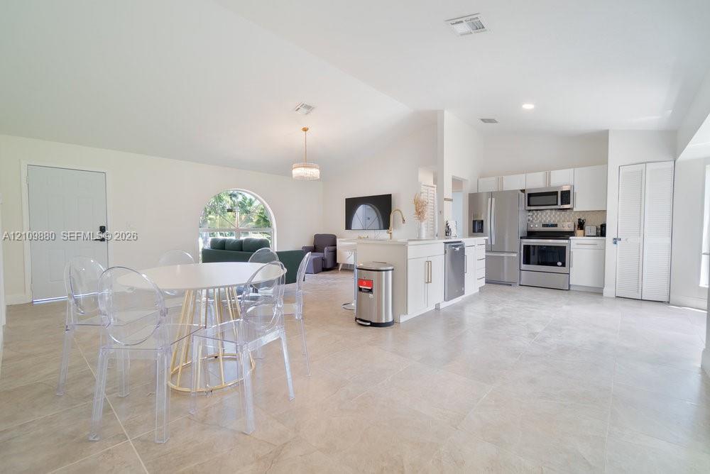 Open floor plan featuring vaulted ceilings, neutral large-format tile flooring, a kitchen island with white cabinetry, stainless steel appliances, and an arched window
