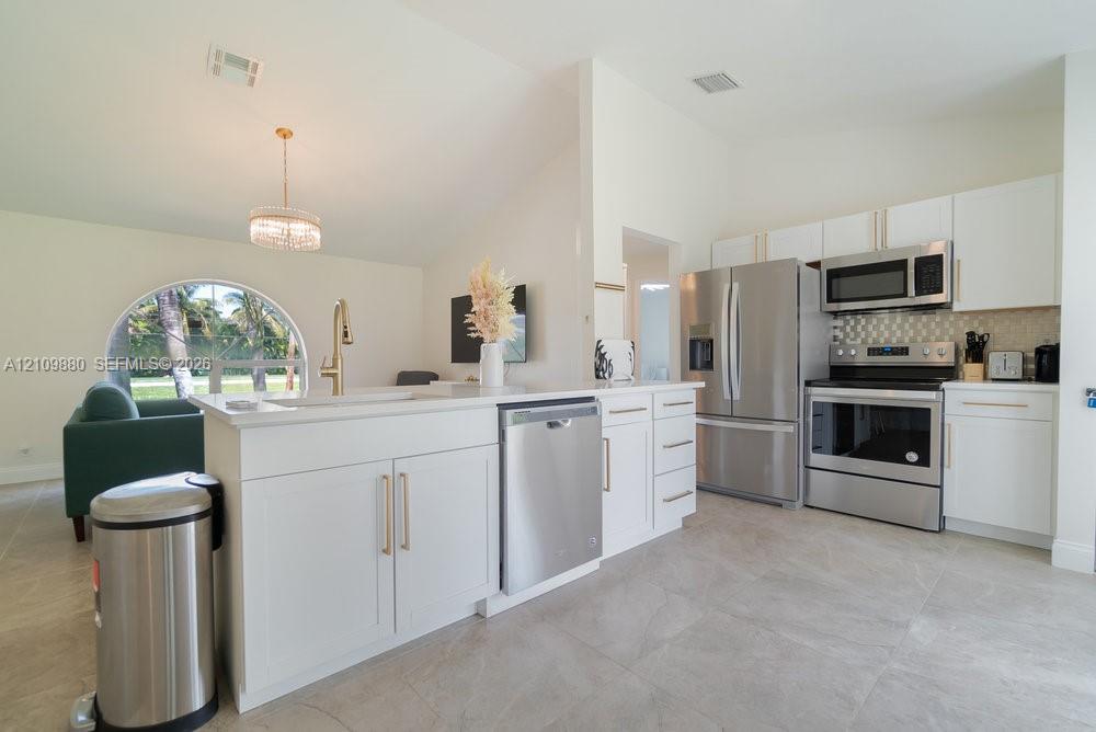 Kitchen featuring white shaker cabinetry, stainless steel appliances, large-format tile flooring, a breakfast bar, and a vaulted ceiling with a circular window