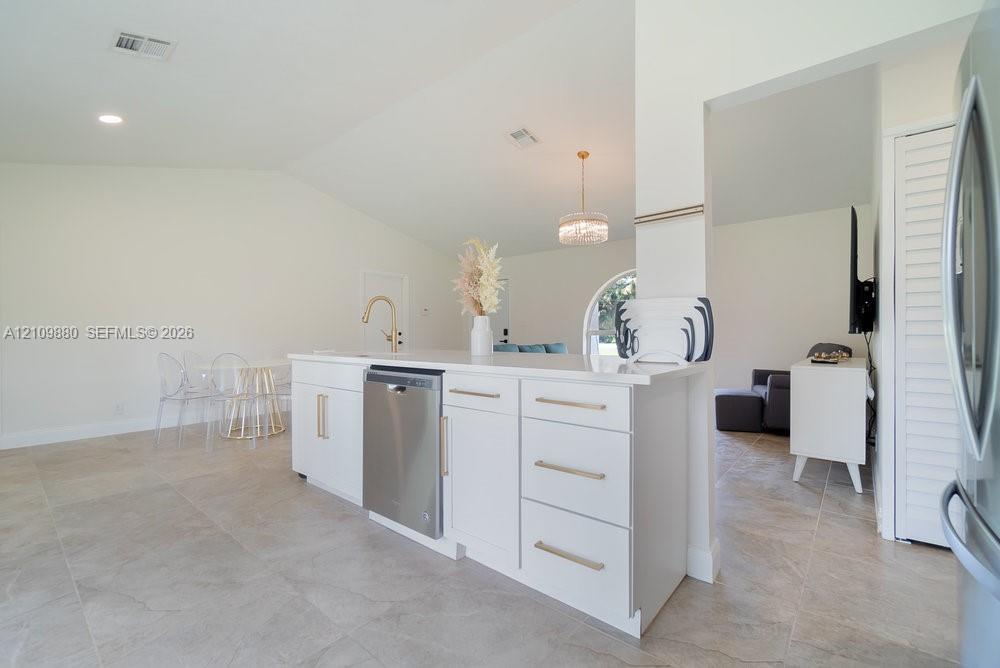 Kitchen island featuring white shaker-style cabinetry, quartz countertops, a brass faucet, and a stainless steel dishwasher, complemented by tile flooring